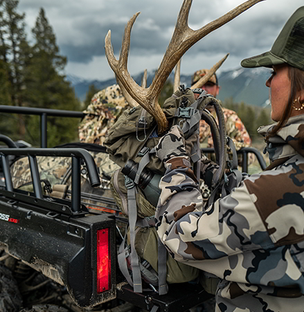 A female hunter grabbing gear from the cargo box of a 2027 Polaris Sportsman 6x6 600 2-up ATV.