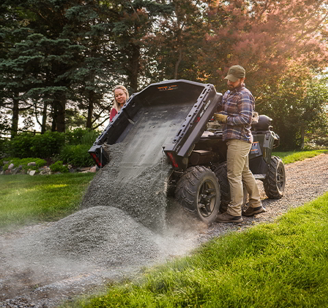 A couple dumping pea rocks out of the cargo box of a 2027 Polaris Sportsman 6x6 600 2-up ATV.