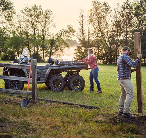 A couple putting up fence posts with gear from the cargo box of their 2027 Polaris Sportsman 6x6 600 2-up ATV.