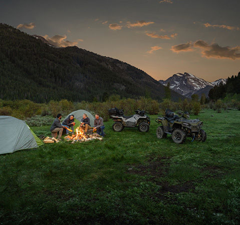 4 people sitting around a campfire near their 2027 Polaris Sportsman Touring 600 2-up ATVs.