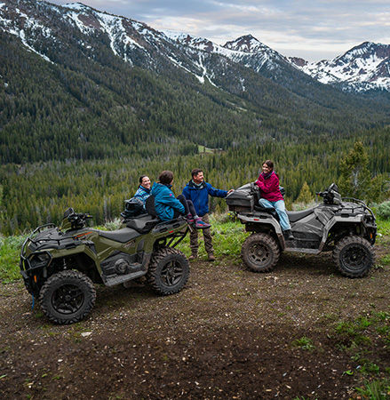 4 people relaxing after a ride on their 2027 Polaris Sportsman Touring 600 2-up ATVs.