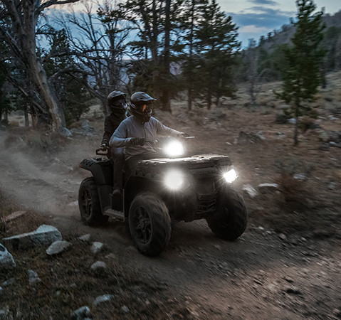 2 riders on a 2027 Polaris Sportsman Touring 850 Premium 2-up ATV with headlights illuminated.