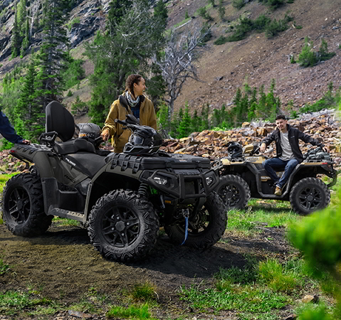3 people relaxing after a trail ride on their 2027 Polaris Sportsman Touring XP 1000 Trail 2-up ATVs.