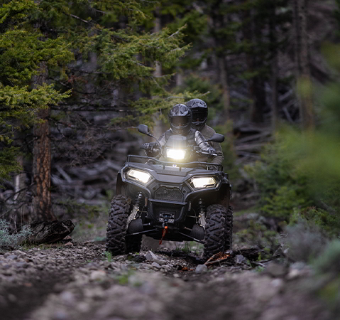 2 riders on a 2027 Polaris Sportsman X2 600 2-up ATV with illuminated headlights.