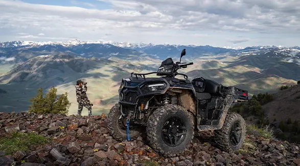 A hunter looking over a ridge near their 2027 Polaris Sportsman X2 600 2-up ATV.