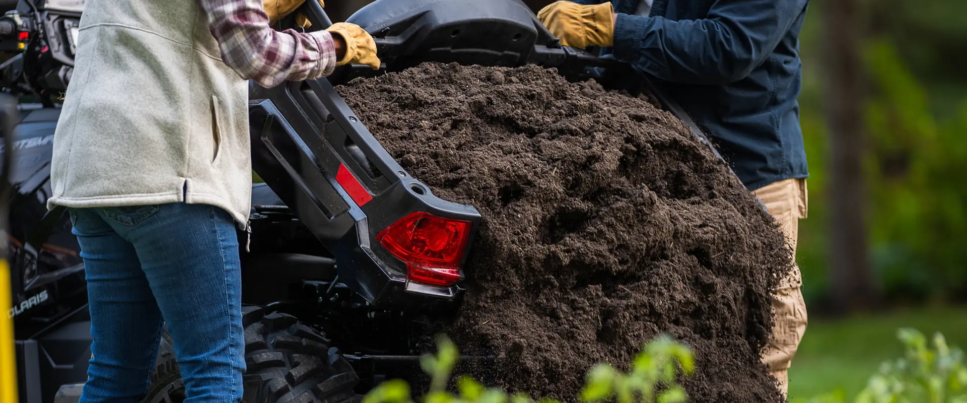 A couple dumping dirt from the cargo box of a 2027 Polaris Sportsman X2 600 2-up ATV.