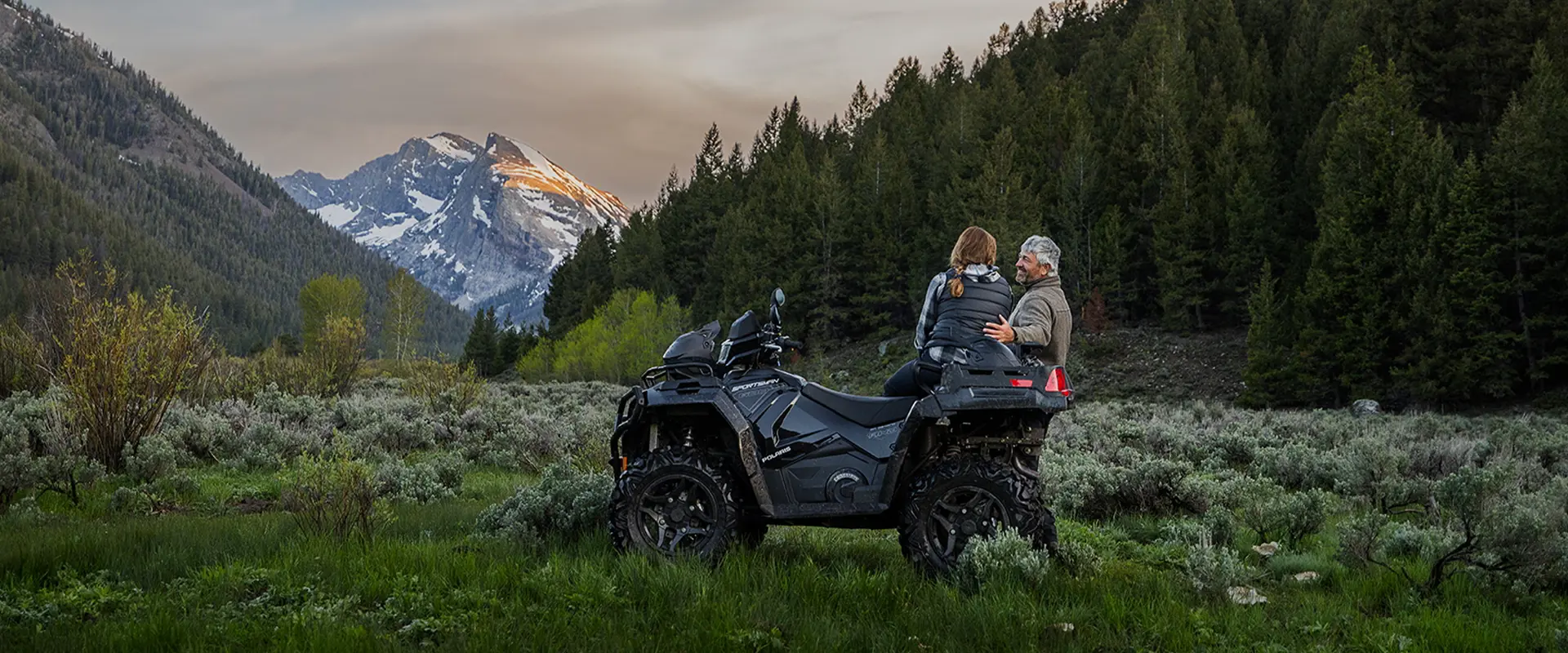 A couple looking toward a mountain at sunset on their 2027 Polaris Sportsman X2 600 2-up ATV.