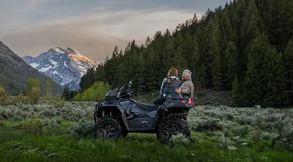 A couple looking toward a mountain at sunset on their 2027 Polaris Sportsman X2 600 2-up ATV.