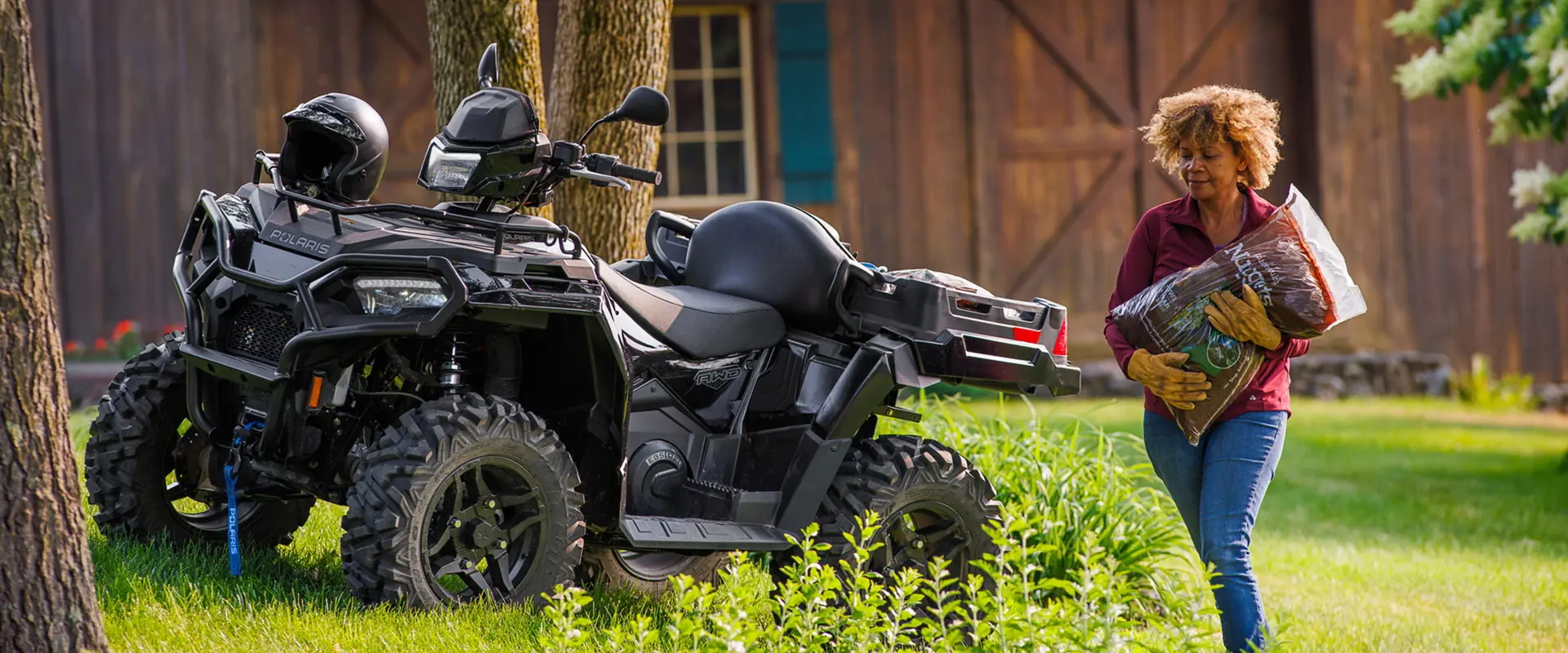 A woman grabbing mulch from the cargo box of a 2027 Polaris Sportsman X2 600 2-up ATV.