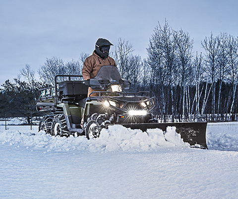 A man clearing the snow from the road using the plow attachment on his sportsman