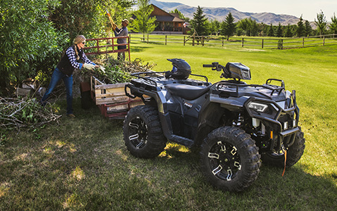 A woman loading branches to the trailer attached to her Sportsman while doing yard clean up