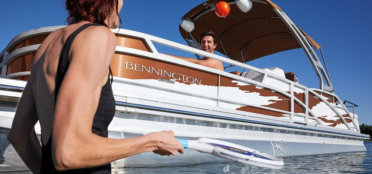 A man looking at a woman playing water tennis next to a Bennington R Bowrider Pontoon Boat