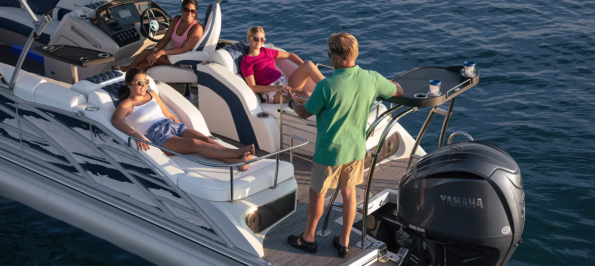people relaxing on the stern lounge seats on a Bennington R pontoon while a man stands on the stern and speaks to them