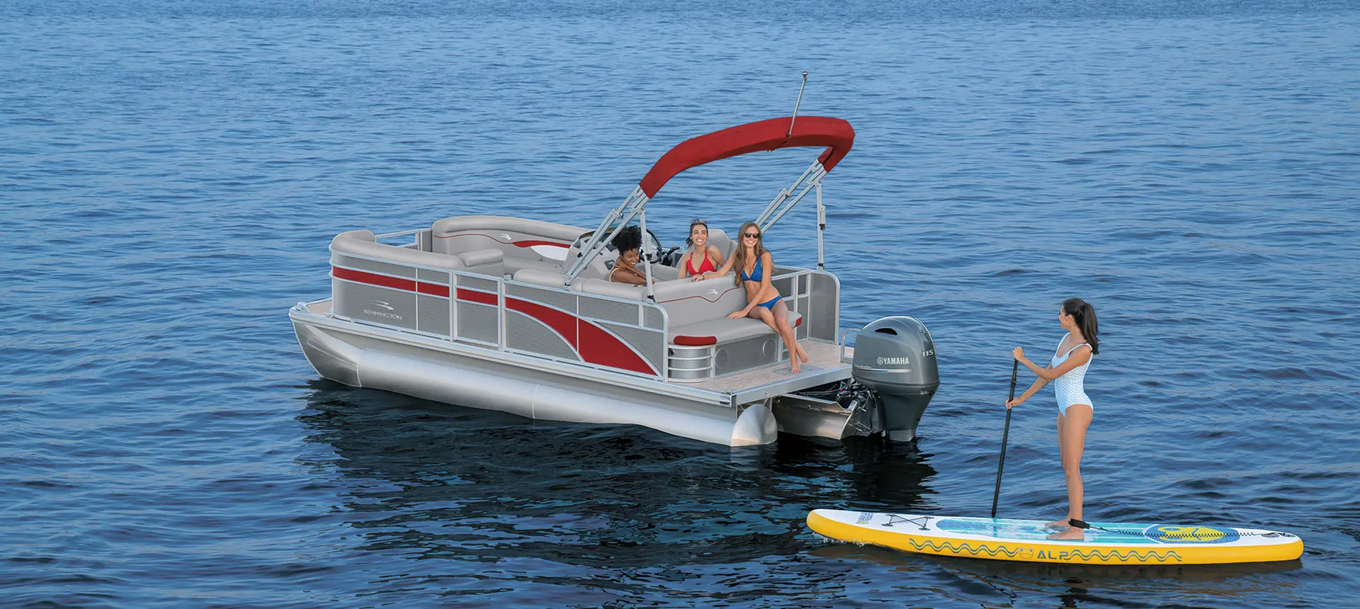 woman stand up paddle boarding near the stern of a bennington s pontoon boat
