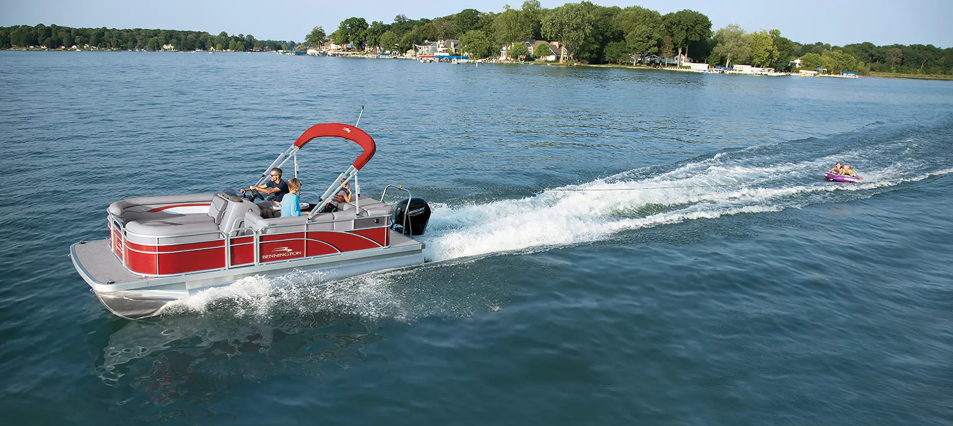 side view of a red Bennington SV pontoon boat pulling a tube on a lake