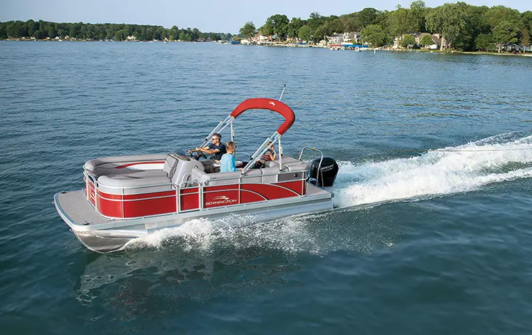 side view of a red Bennington SV pontoon boat pulling a tube on a lake