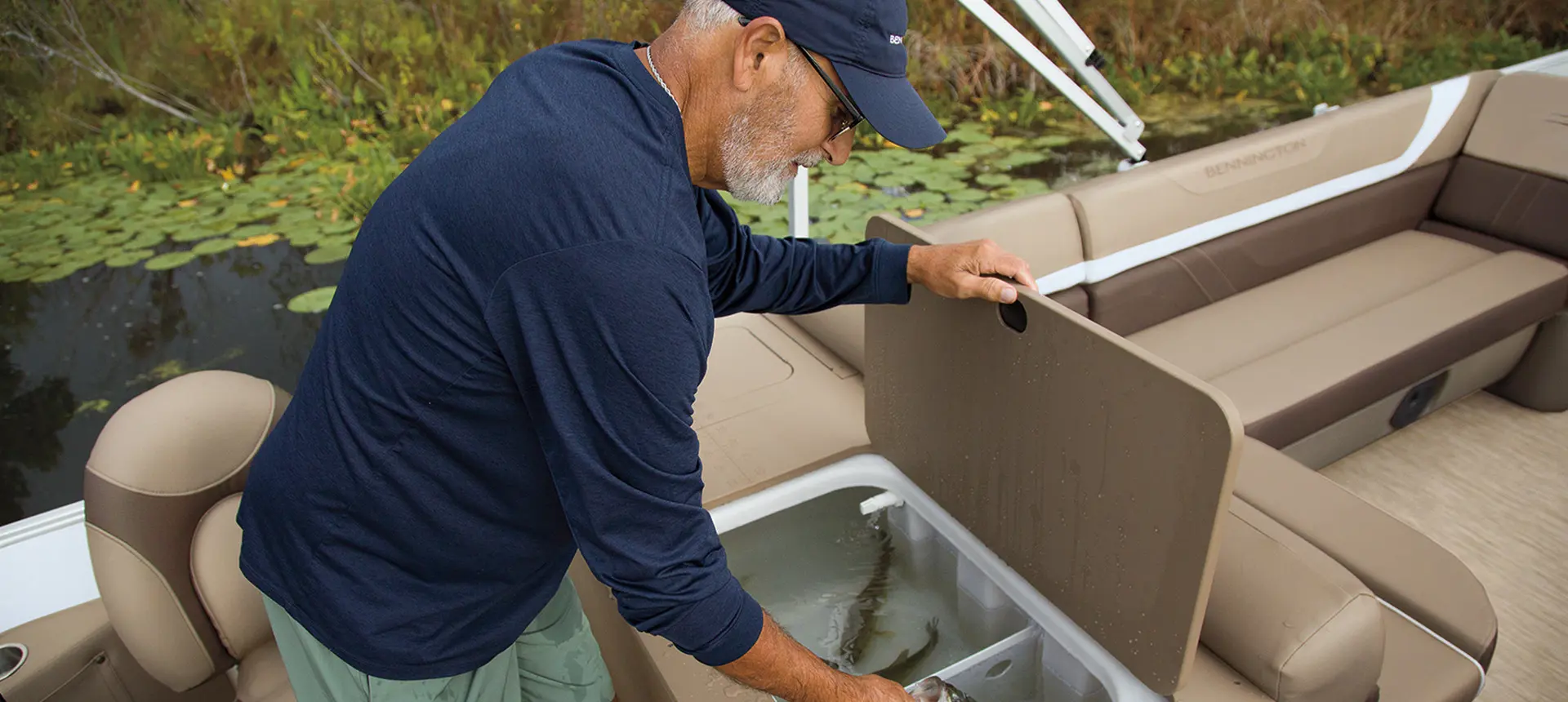 A man placing a fish inside the integrated livewell on a Bennington SX pontoon boat