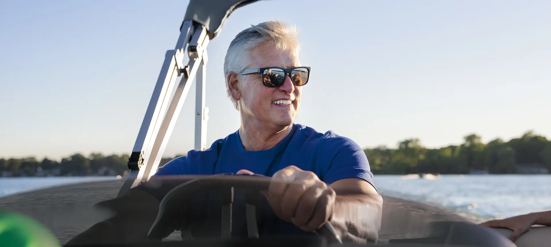 man at the helm of a Bennington S pontoon boat on a lake