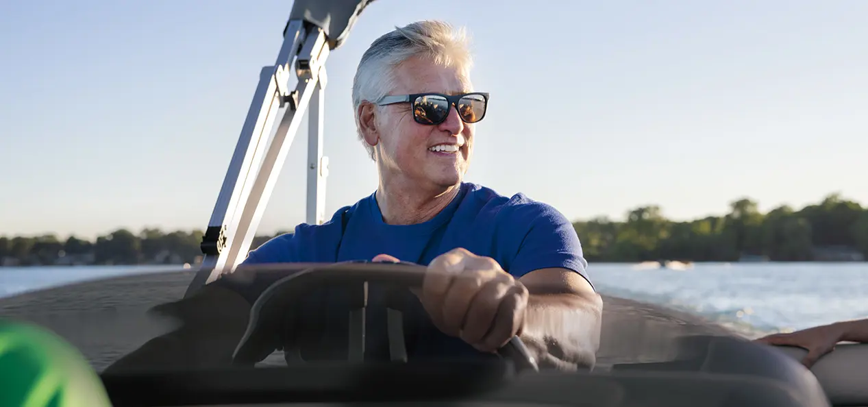 man at the helm of a Bennington S pontoon boat on a lake
