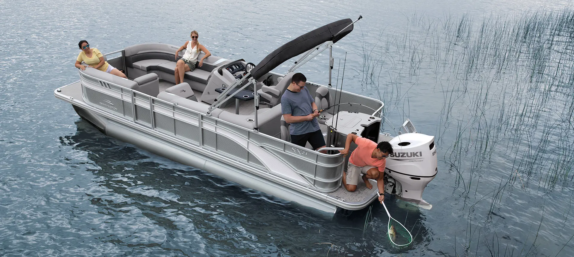 man using a net to grab a fish another mac caught from the stern of a bennington sx pontoon boat