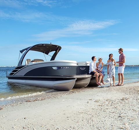 Four people relaxing near a beached Bennington saltwater pontoon.