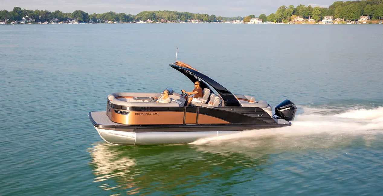 Side profile of a Bennington LX Sport pontoon boat cruising across a lake.