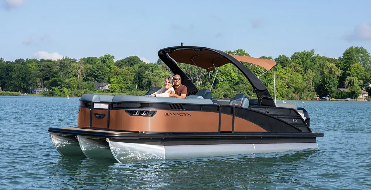 A couple smiling from the bow seating on a Bennington LX Sport pontoon boat.