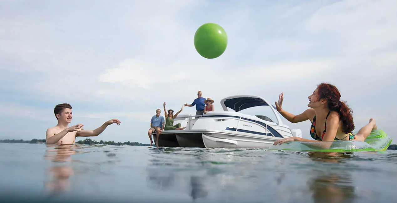 Kids playing with a ball in the water while their parents watch in the background from the comfort of their Bennington Q Line pontoon boat.
