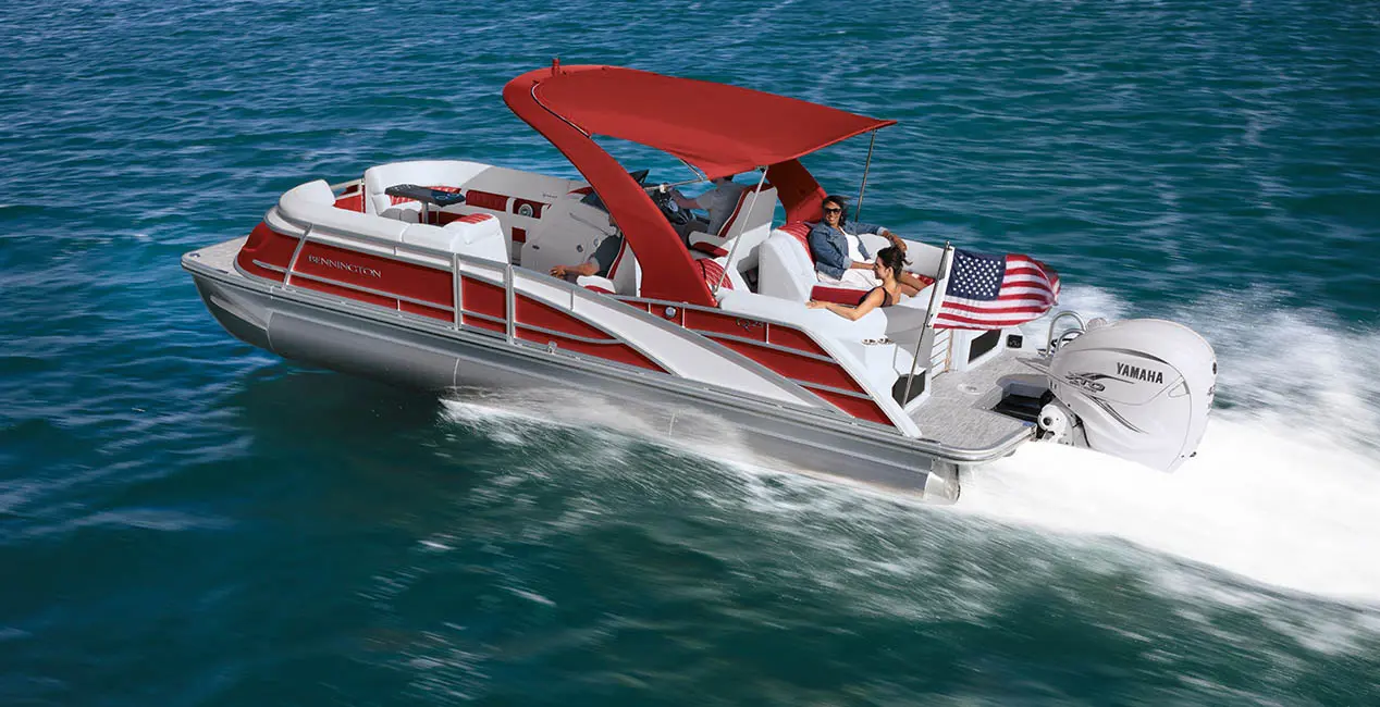 Side view of a red Bennington Q Line pontoon boat cruising on a lake.