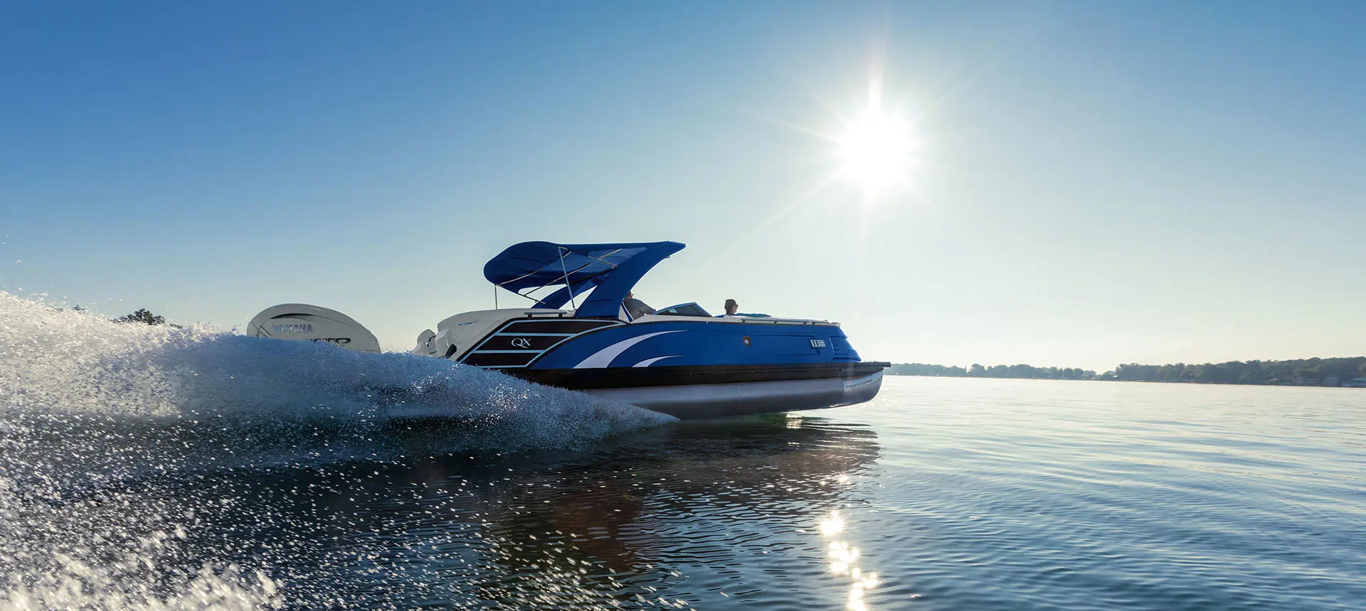 Side profile of a Bennington QX Line pontoon boat making waves on a lake.