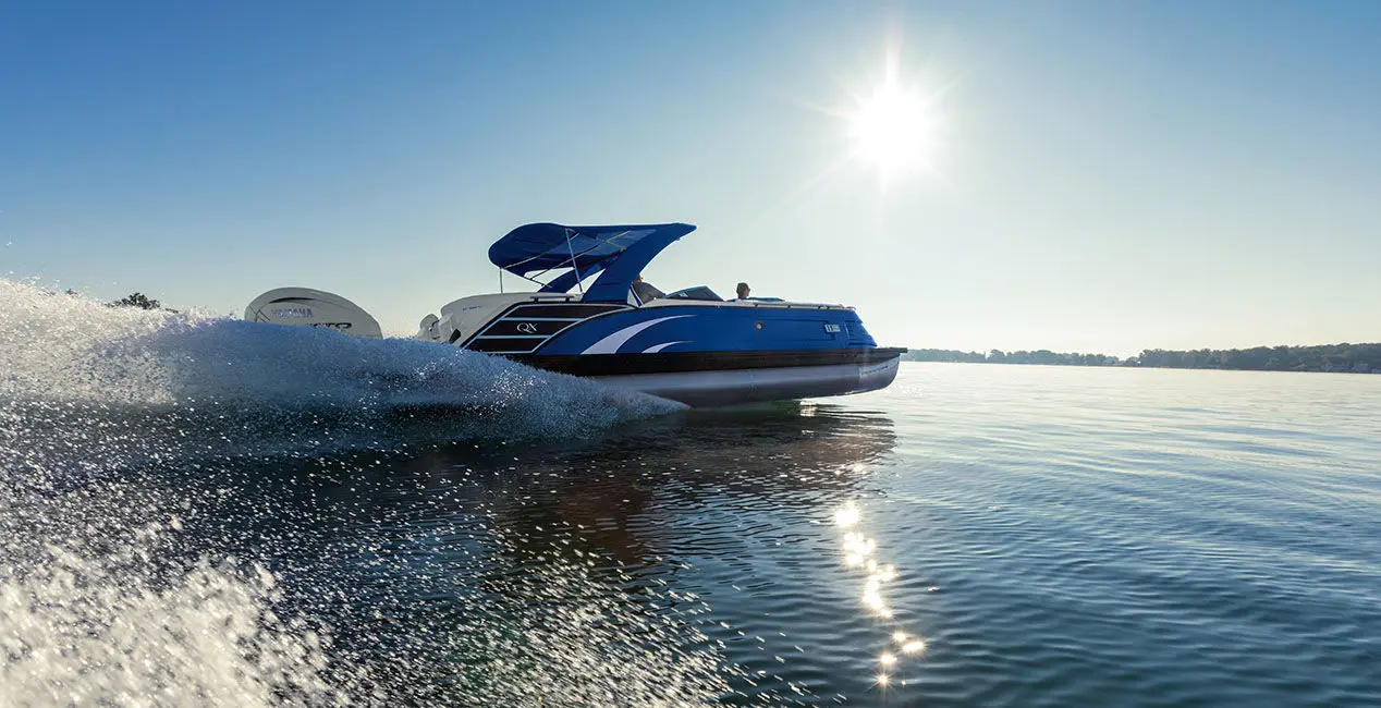 Side profile of a Bennington QX Line pontoon boat making waves on a lake.