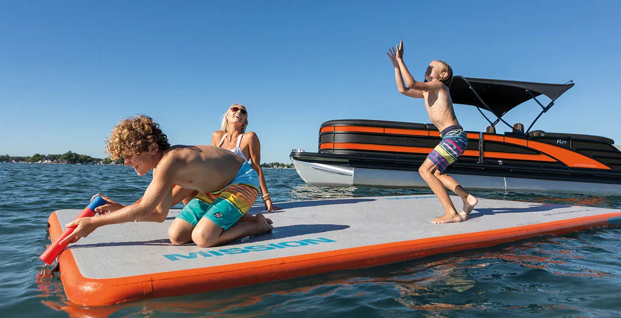 Famille jouant sur un tapis flottant avec un bateau ponton Bennington R Line en arrière-plan.