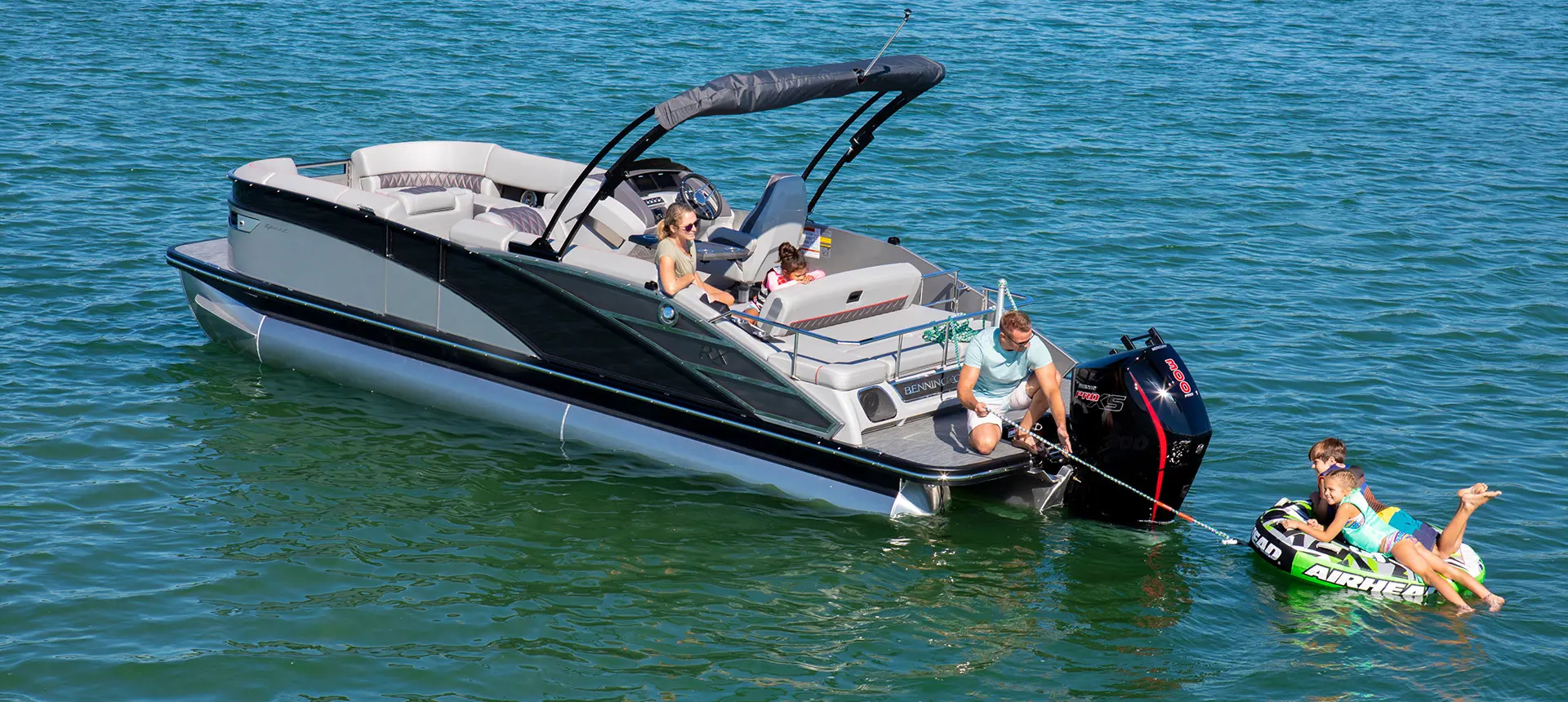 Man pulling in a tub with 2 kids on it from the stern of a Bennington RX Sport pontoon boat.