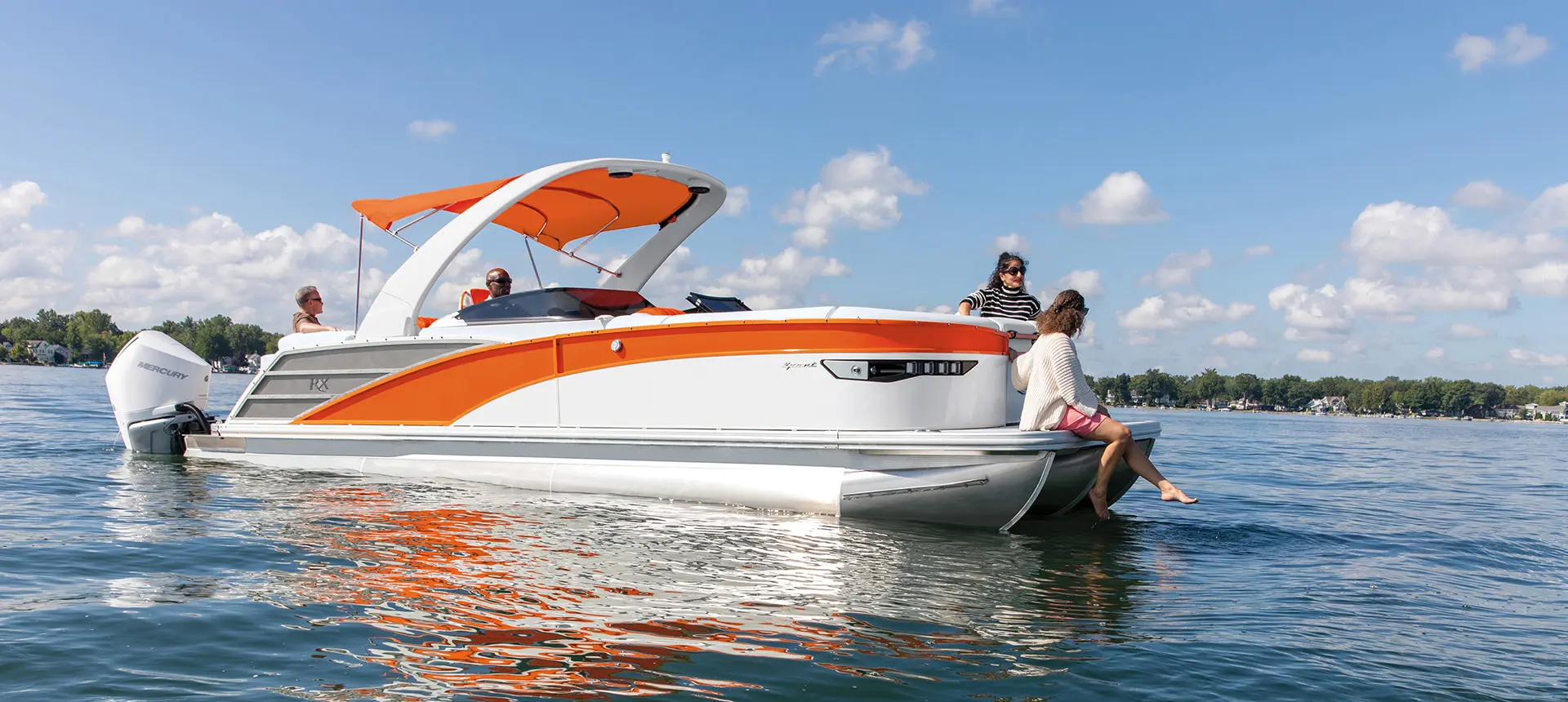 Side profile of a Bennington RX Sport pontoon boat with a woman sitting on the bow with her feet in the water.