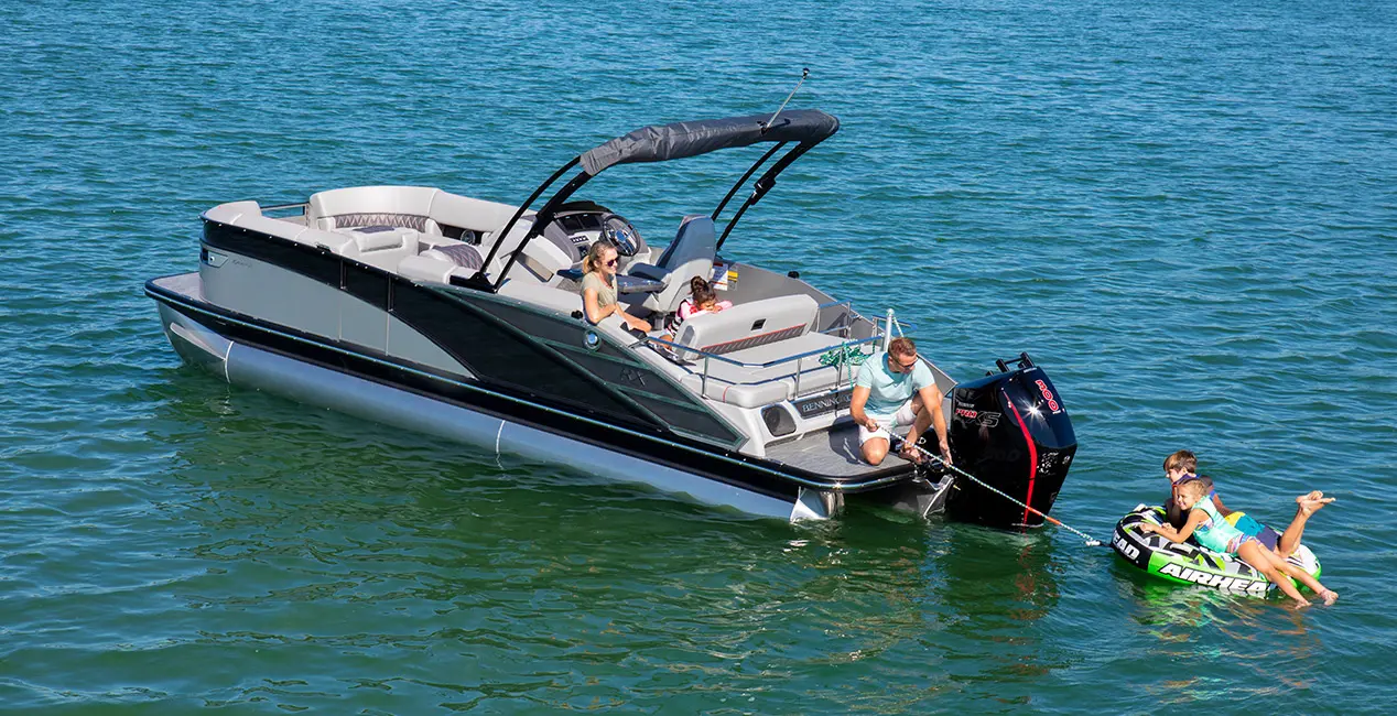Man pulling in a tub with 2 kids on it from the stern of a Bennington RX Sport pontoon boat.