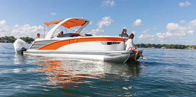 Side profile of a Bennington RX Sport pontoon boat with a woman sitting on the bow with her feet in the water.