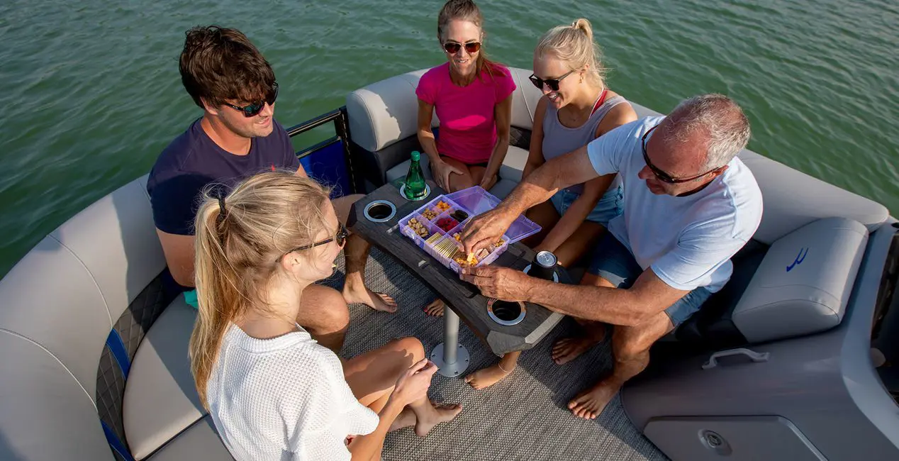 Family enjoying a snack at the bow table on a Bennington SX Line pontoon boat.