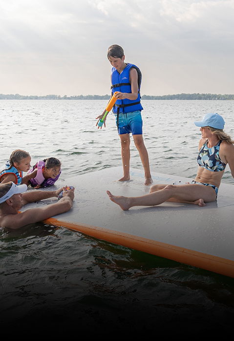 Famille profitant d’un grand tapis de bain gonflable à côté d’un ponton Bennington sur un lac.