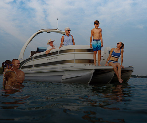 Family hanging out in water towards the front of a parked Bennington Pontoon Boat. 