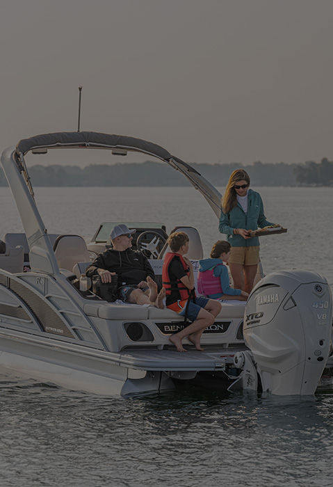 Family smiles on dock while wearing Bennington apparel and loading cooler into pontoon boat.