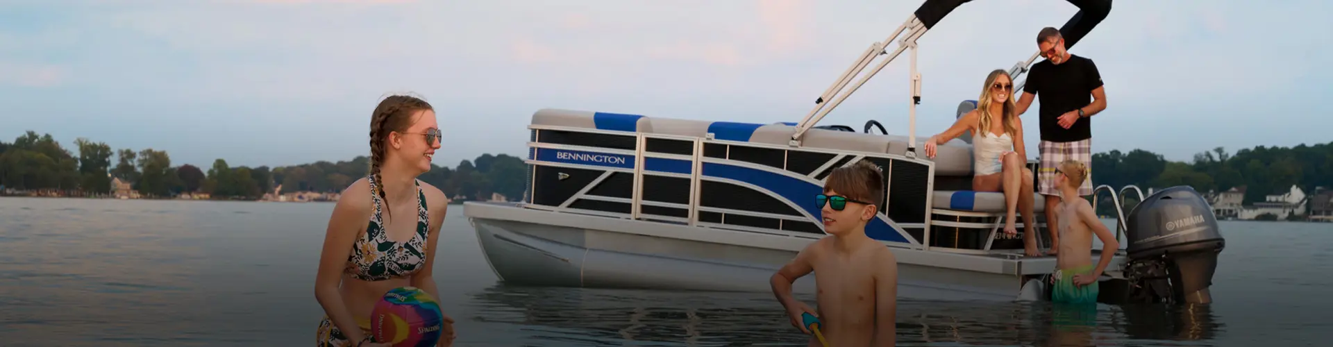Family playing in shallow water near a parked pontoon boat. 