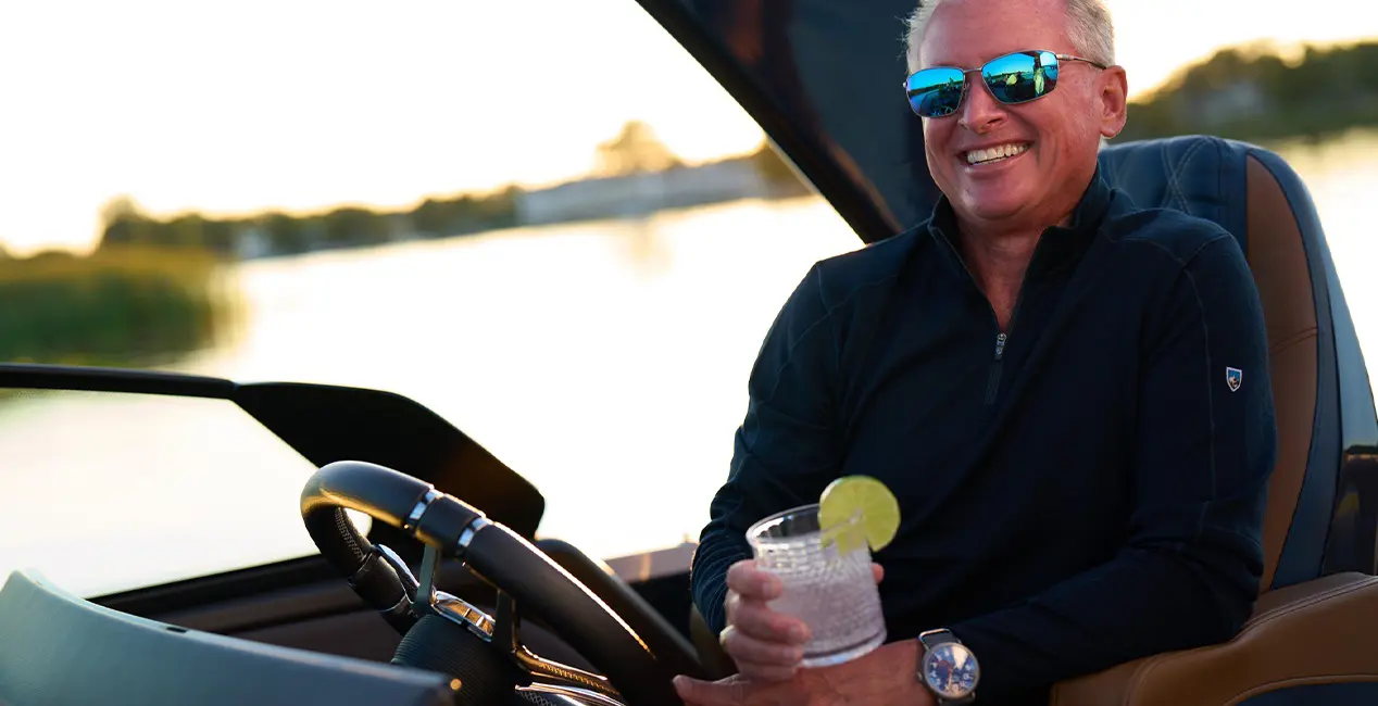 A man smiling at the helm of a Bennington QX line pontoon boat.