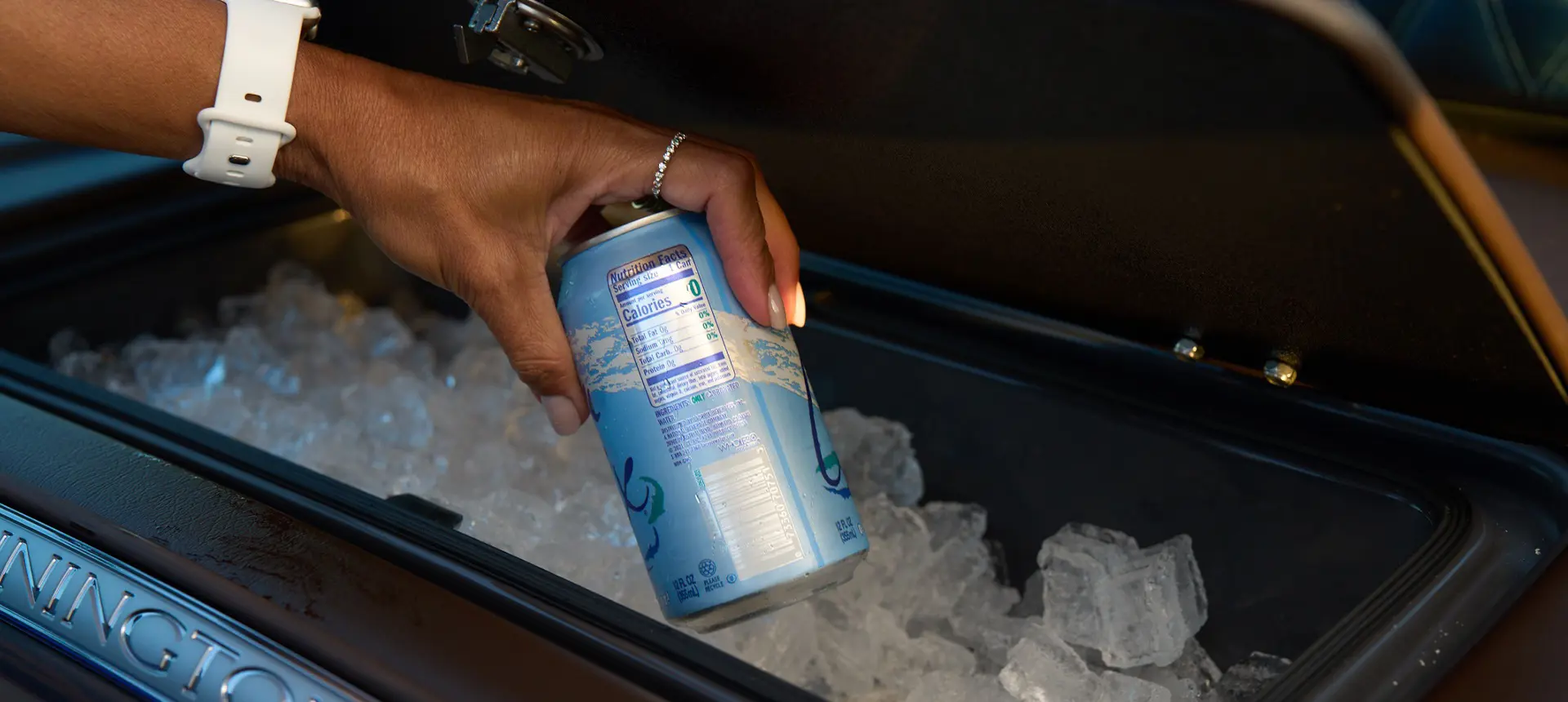 A person grabbing a canned beverage from an integrated cooler on a Bennington QX line pontoon boat.