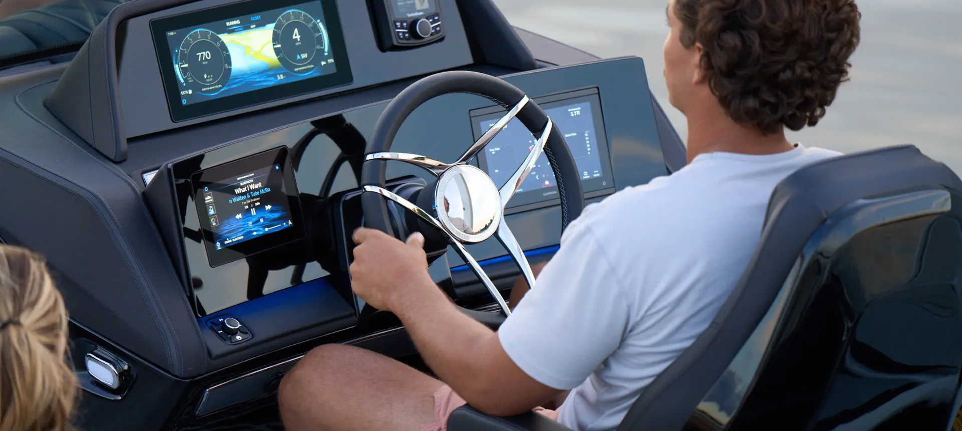 A person at the helm steering a Bennington QX line pontoon boat across a lake.