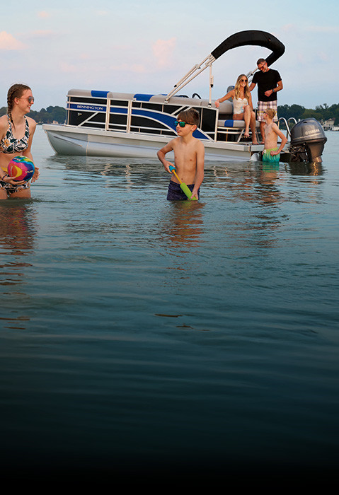 Family playing at sunset in lake behind a Bennington S One Pontoon boat. 
