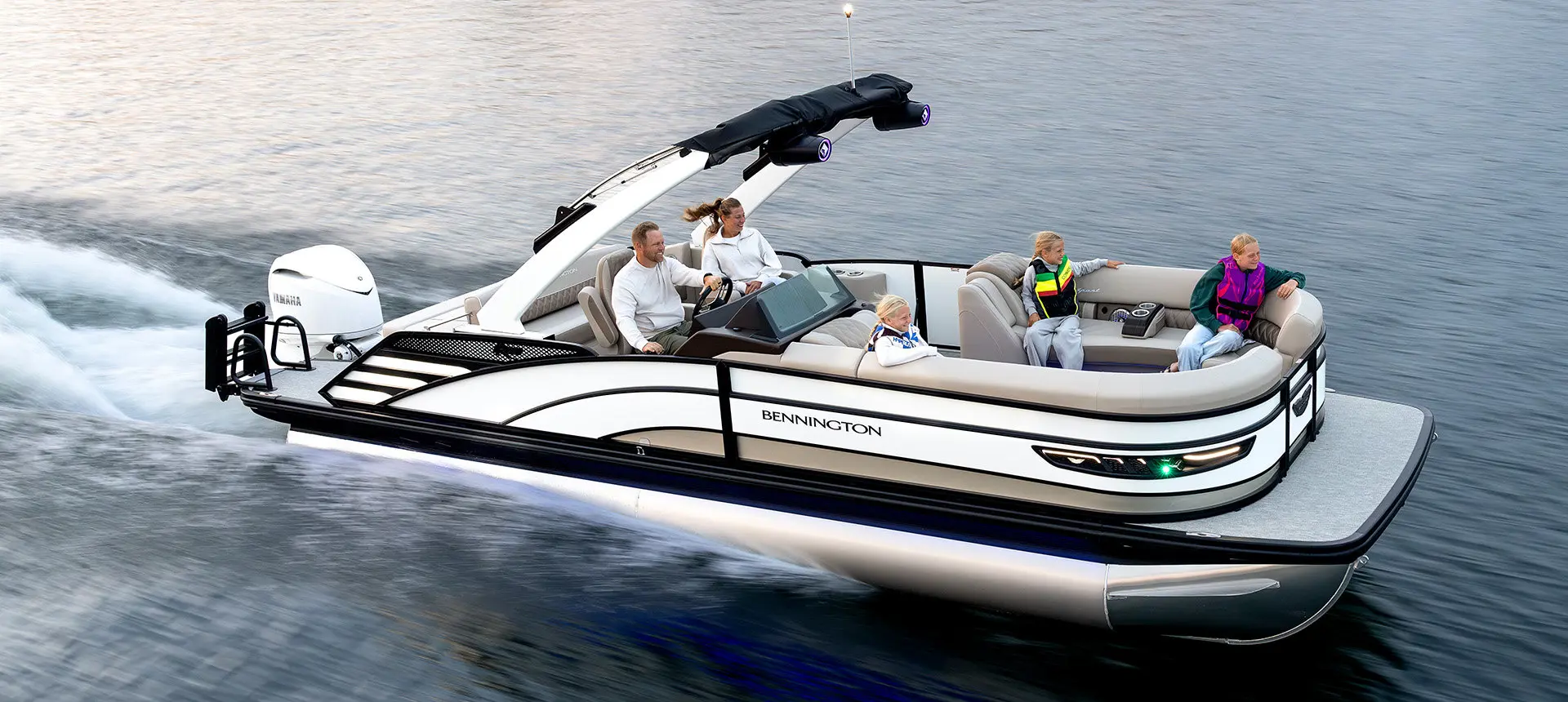 Side profile of a Bennington R Line pontoon boat cruising across a lake.