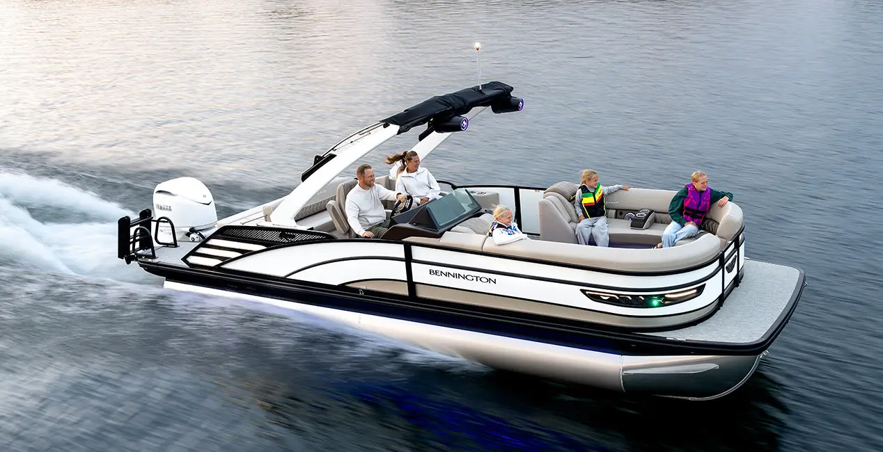 Side profile of a Bennington R Line pontoon boat cruising across a lake.
