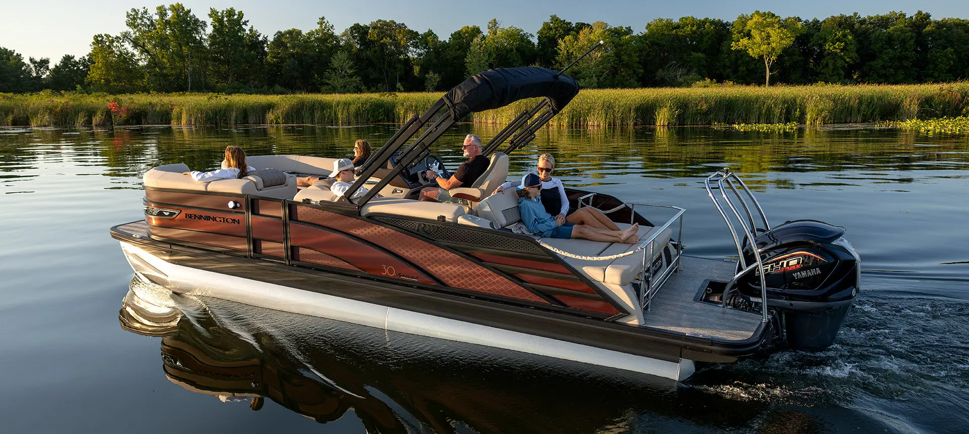 Side profile of a Bennington R Line pontoon boat cruising across a lake.