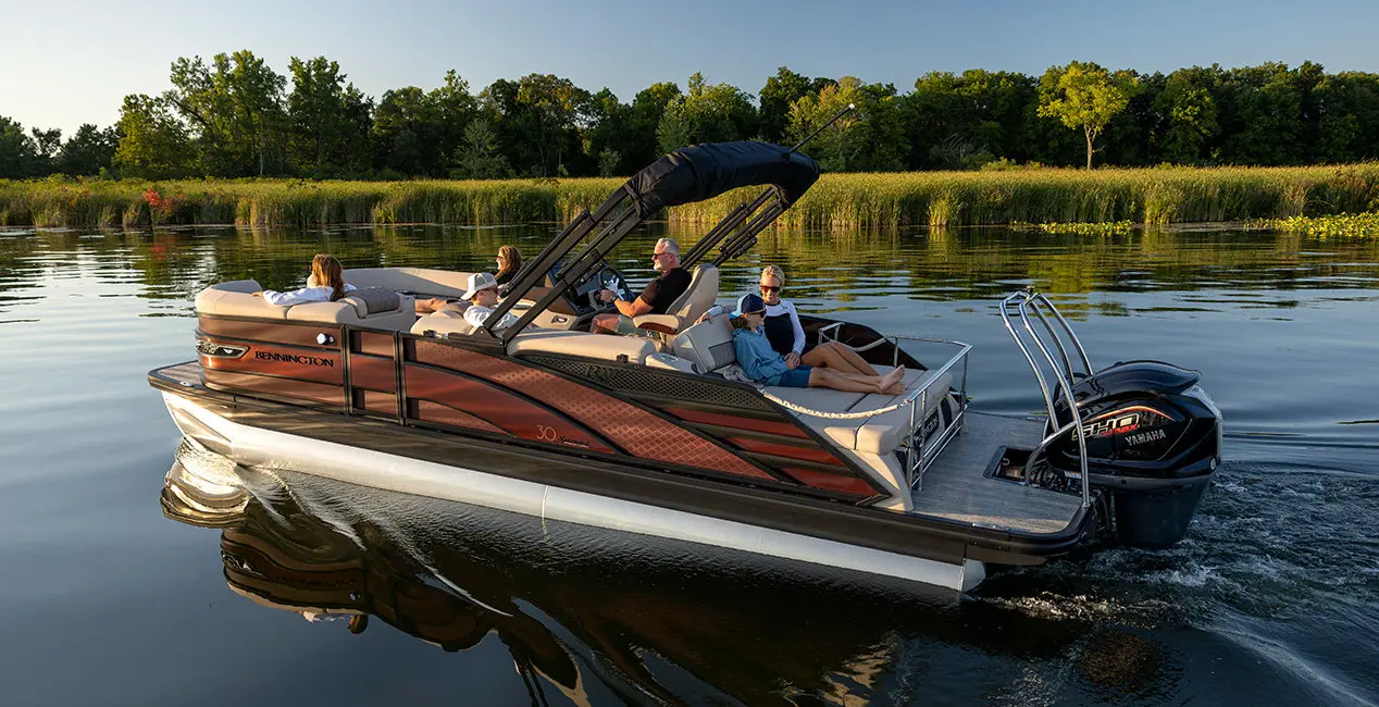 Side profile of a Bennington R Line pontoon boat cruising across a lake.
