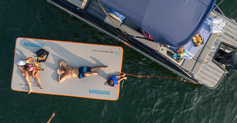 Overhead view of a family relaxing on a floating inflatable mat near a parked Bennington pontoon.
